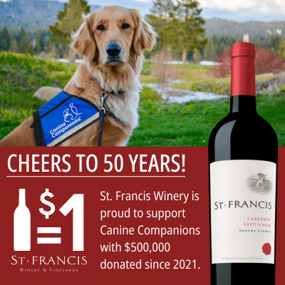 A golden retriever wearing a blue vest that reads 'Canine Companions' sits in front of a picturesque natural background. Next to the dog is a bottle of St. Francis Cabernet Sauvignon, with a promotional message celebrating the winery's $500,000 support for Canine Companions since 2021.